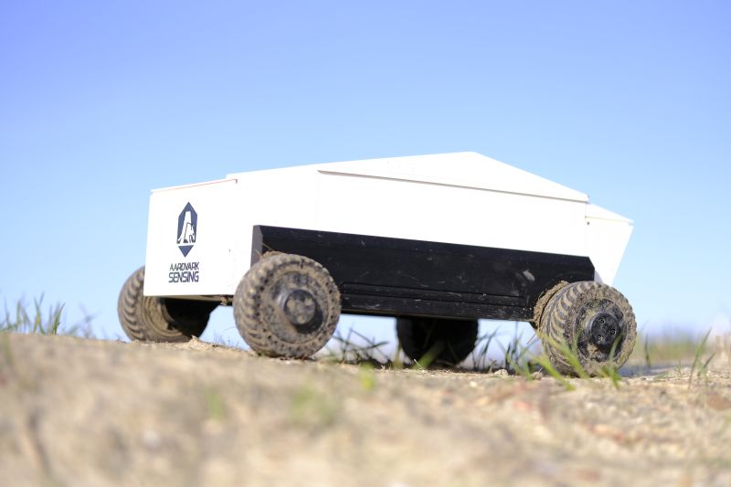 white autonomous robot driving across rough, muddy terrain