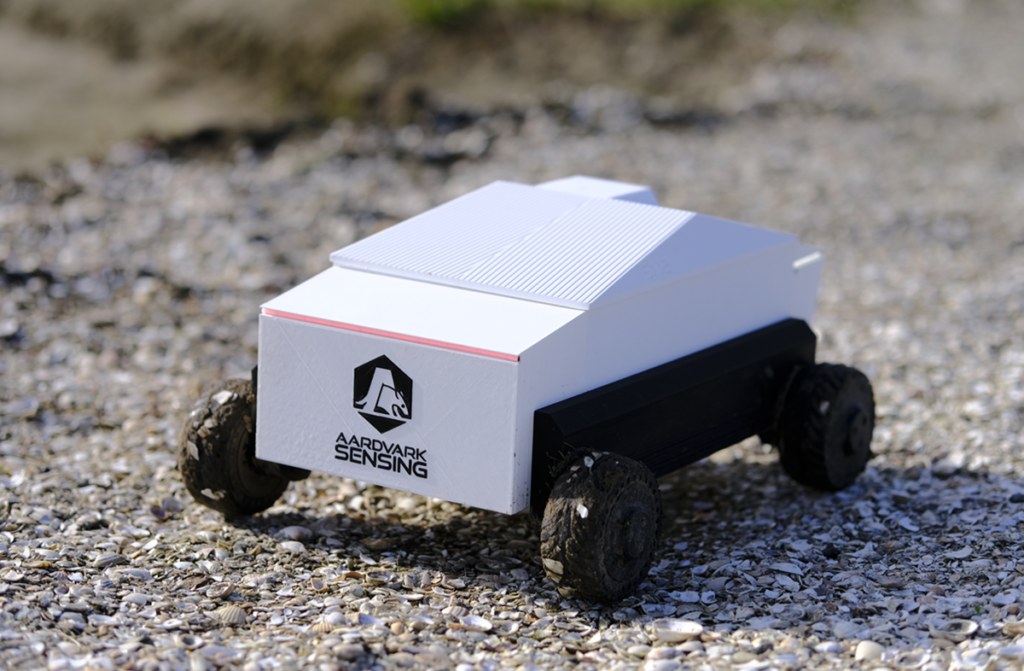 white autonomous robot with black wheels driving across rough, muddy terrain