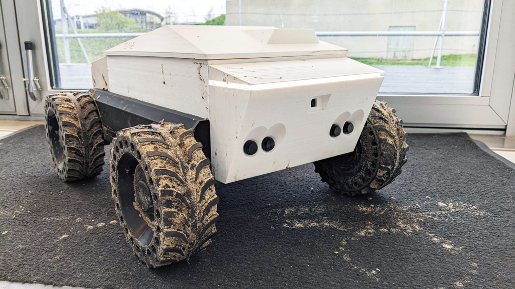 white autonomous robot with big wheels cassette, muddy after driving across rough terrain