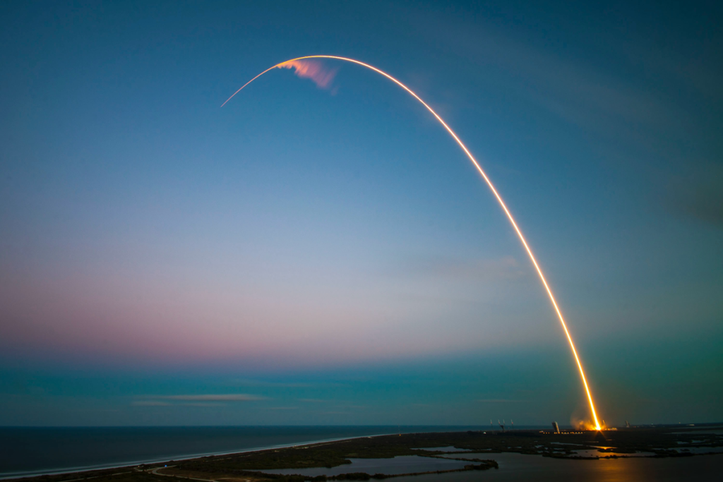 ray of light near body of water following rocket launch into a clear sky